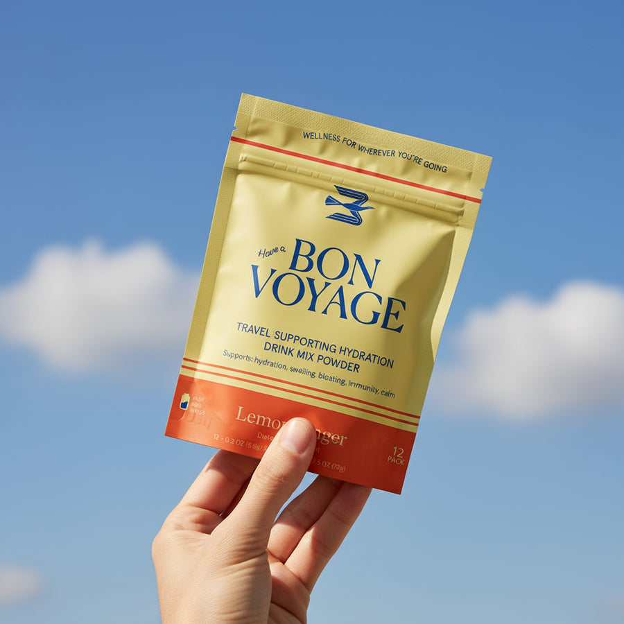 Hand holding a 'Bon Voyage' drink mix powder packet against a blue sky background